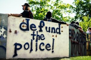 Unrecognizable people near graffiti wall in city park during strike says defund the police