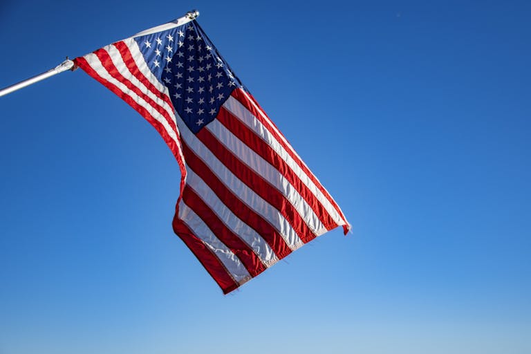 The American flag proudly waves on a flagpole against a clear blue sky, symbolizing freedom and patriotism.